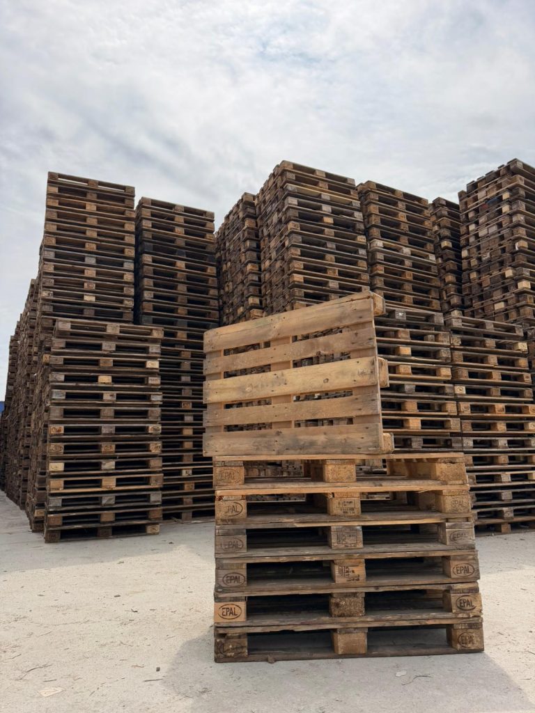 Stivă de paleți din lemn, marcați EPAL, amplasați într-un spațiu industrial exterior, cu turnuri înalte de paleți depozitați în fundal. Logistică, retail, producție