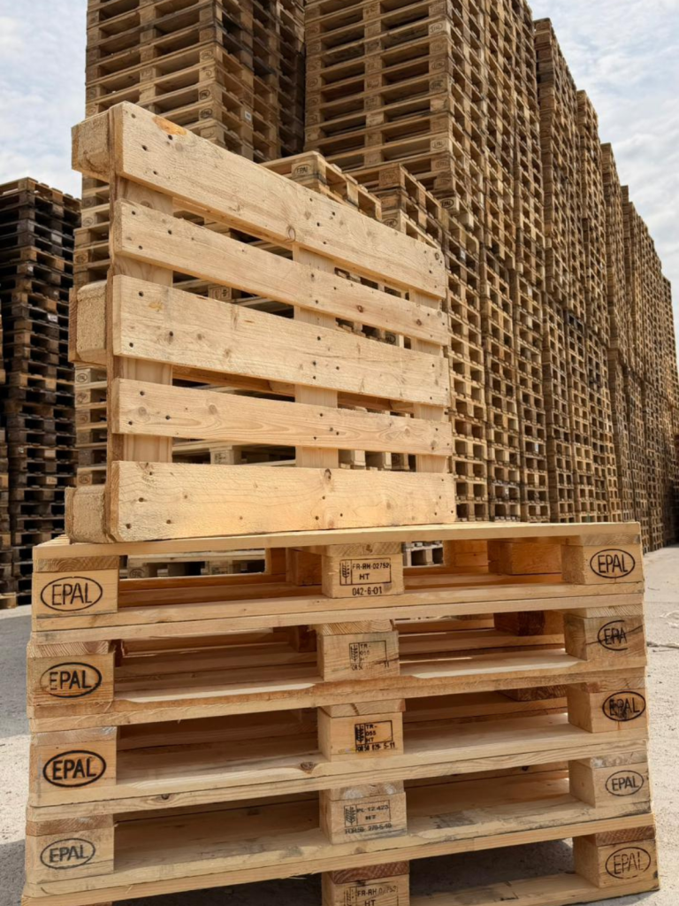 Stivă de paleți din lemn, marcați EPAL, amplasați într-un spațiu industrial exterior, cu turnuri înalte de paleți depozitați în fundal. Logistică, retail, producție